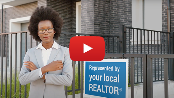 a dark skinned woman stands confidently in front of a house with a for sale sign